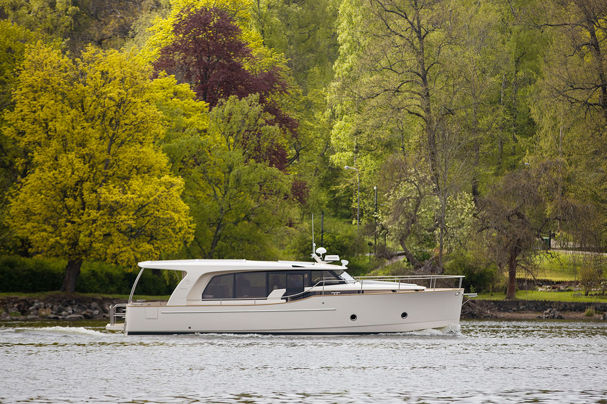 En vit yacht ute på en sjö där en naturmiljö syns i bakgrunden